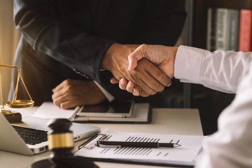 When should your business hire a lawyer in Monroe, LA? Niswanger Law. Image of business person and business lawyer shaking hands after discussing contract papers.